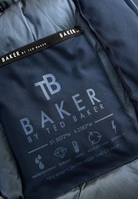 Indvendigt label i marineblå pufferjakke med hvid tekst og ikoner, der angiver specifikationer: vandafvisende, holdbar, varm, genanvendt fyld.