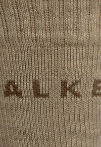Calcetín de punto beige con textura acanalada y letras marrones. El diseño es sencillo, con un enfoque en la comodidad y la calidez.