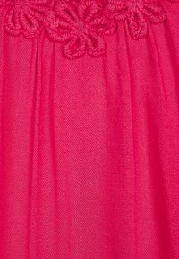 Rosa tyg med broderade blommor längs toppen, med en texturerad finish och veckad design.