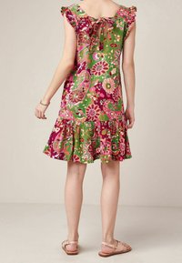 Vestido de estampado floral hecho de una tela ligera, con mangas con volantes, un lazo en la espalda y un dobladillo con volantes. Los colores predominantes son verde y rosa.