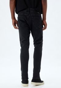 Jeans negros ajustados con una textura suave, con bolsillos traseros y una cintura de altura media, combinados con zapatillas negras.