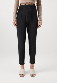 Černé kalhoty s vysokým pasem a páskem, zúžené nohavice a ohrnuté manžety; spárované s béžovými pantoflemi s otevřenou špičkou. Hladká textura látky.