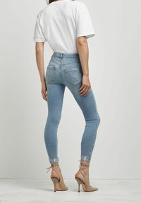 Jeans de tiro alto en azul claro con un ajuste ajustado, dobladillo sin terminar y bolsillos traseros, combinados con una camiseta blanca simple y tacones altos beige.
