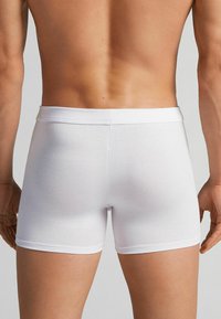 Weiße Baumwoll-Boxershorts mit einem weichen, elastischen Taillengummi, passgenauem Design und glatter Textur, die die Rückansicht und die Seite eines Beins zeigen.
