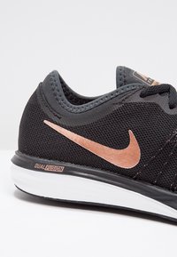Musta urheilujalkine, jossa on verkkomateriaali, rose gold Nike -logo ja "DUAL FUSION" -merkintä. Varustettu valkoisella välipohjalla ja teksturoiduilla yksityiskohdilla.
