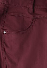 Burgundy bomullstyg med en slät yta, med en sidoficka och silverfärgade metallaccenter vid fickan.