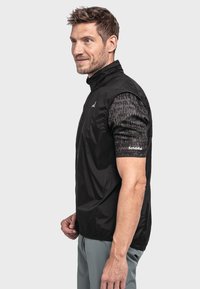 Schwarze leichte Jacke mit kurzen gemusterten Ärmeln. Verfügt über einen Stehkragen und ein Logo auf dem Ärmel. Glatte, synthetische Textur.