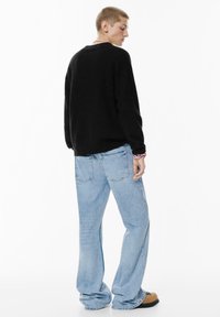Maglione nero con scollatura a girocollo, abbinato a jeans azzurri larghi. L'outfit presenta una silhouette rilassata e un design minimalista.