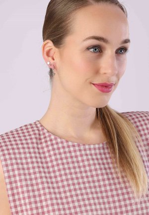Silver star earrings with a polished finish, worn by a model with long hair. Light gingham patterned top in pink and white.