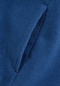Blauwe fleece stof met een zachte, textuur oppervlak. Heeft een diagonale naad en een open zak-detail.