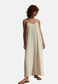 Maxikleid aus weichem, strukturiertem Creme-Stoff, mit lockerer Passform, Spaghettiträgern und gerafftem Ausschnitt. Getragen mit flachen Sandalen.