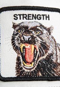 Parche bordado que presenta el rostro de un animal feroz con la boca abierta, detalle en negro, marrón y rojo, bordeado con hilo negro, etiquetado como "FUERZA".