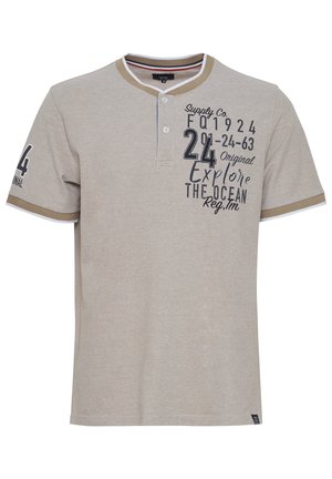 Polo beige de tela suave, con cuello abotonado y detalles en contraste. Incluye texto y números impresos en tinta oscura.
