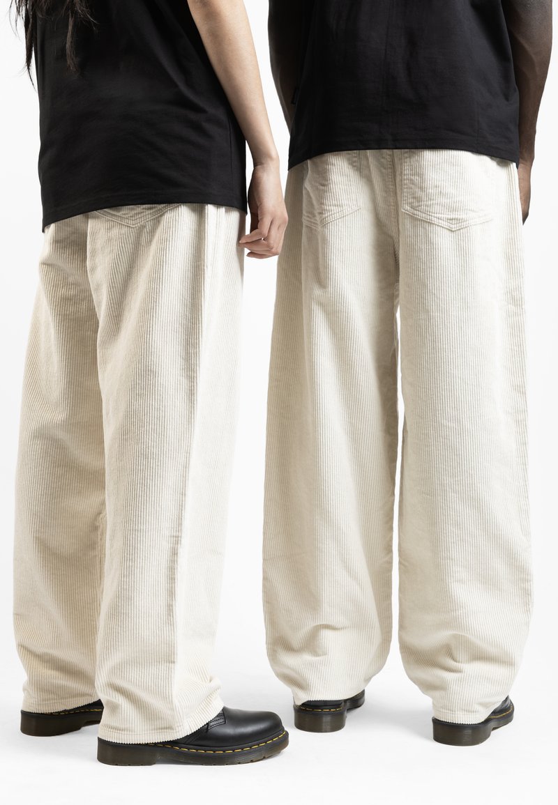 Wide-leg corduroy pants in off-white with vertical stripes, featuring a loose fit and two back pockets. Black platform shoes complete the look.