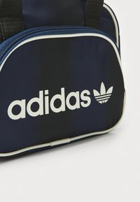 Adidas duffle bag in navy blue fabric, featuring white logo and accents, with a textured surface and prominent zip closure at the top.