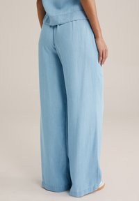 Ljust blå vida byxor i mjuk denim, med hög midja och en ren finish vid fållen utan synliga knäppningar.