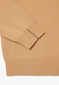 Maglione a maglia beige con polsini e orlo a coste, con un dettaglio verde sul polsino. Texture liscia, design casual.