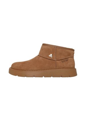 Stivaletto in camoscio marrone con suola spessa in gomma, logo metallico a forma di cuore sul lato e marchio "Skechers Supins" vicino al tallone.