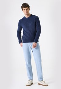 Navyblauer Rundhals-Pullover aus weichem Material, kombiniert mit hellblauen Jeans und weißen Sneakers mit braunen Akzenten.