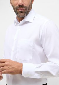 Witte langslijfshirt met een borstzak, knoopsluiting en puntige kraag. Glad materiaal met een klassiek ontwerp.