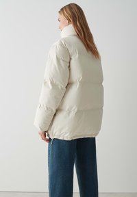 Giubbotto piumino beige chiaro, con colletto alto, design trapuntato e polsini elasticizzati, abbinato a pantaloni in denim scuri.