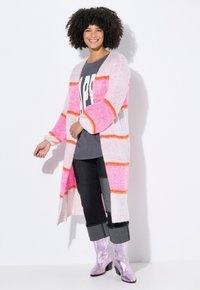 Strick-Cardigan mit rosa, weißen und orangefarbenen Streifen. Lange Ärmel und offenes Vorderteil. Getragen über einem grauen Grafik-T-Shirt und schwarzen Jeans.