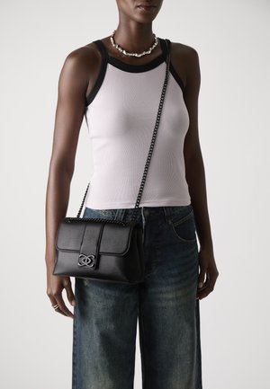 Black leather shoulder bag with a textured finish and a decorative clasp, worn crossbody with a chain strap, paired with a light tank top and jeans.