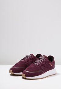 Burgundy sneakers made of suede with gray laces. White midsole and gum rubber outsole. Features three parallel stripes on the side.