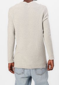 Pull gris clair texturé avec manches longues, encolure côtelée et fentes latérales. Le matériau semble doux et tricoté avec une coupe ample.