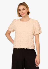 Blusa corta a maniche corte di colore rosa chiaro con un motivo floreale testurizzato. Fit dritto, scollatura rotonda e maniche arricciate. Tessuto morbido.
