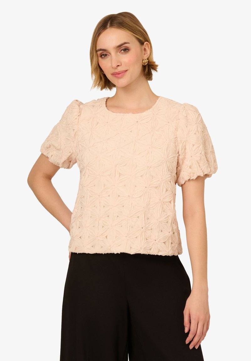 Blusa corta a maniche corte di colore rosa chiaro con un motivo floreale testurizzato. Fit dritto, scollatura rotonda e maniche arricciate. Tessuto morbido.