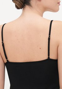 Svart linne med tunna remmar, som har justerbar hårdvara. Slät textur med en enkel design som visar ryggen och axlarna.