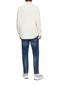 Chemise blanche à manches longues, coupe décontractée, en coton. Associée à un jean en denim bleu, coupe droite, texture délavée et légères déchirures. Baskets blanches.