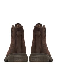 Bottes ankle en daim marron avec une finition lisse, dotées d'une languette en boucle et de semelles en caoutchouc texturé. Marquage subtil sur le talon.