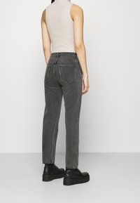 Pantalones vaqueros de mezclilla gris con corte recto, bolsillos traseros visibles y detalles de costura sutiles. Combinados con botas negras de plataforma con cordones.