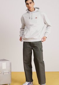 Sudadera de algodón gris con bolsillo canguro frontal y logo pequeño. Pantalones cargo verdes oliva con bolsillos laterales. Zapatillas blancas con detalles en azul.