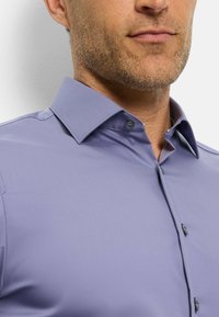 Helllilahe Bluse, glattes Material, klassischer Kragen, durchgehender Knopfverschluss mit dunklen Knöpfen, ordentliche Nähte, ohne Muster oder Akzente.