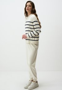 White long-sleeve top with navy horizontal stripes, paired with cream jogger pants and white sneakers, featuring ribbed cuffs.