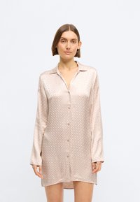 Rochie camă din satin roz deschis, cu o textură subtilă, mâneci lungi, guler și închidere cu nasturi pe față.