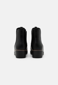 Svarta ankelstövlar med slät läderfinish, elastiska sidopaneler och texturerade gummisulor. Diskreta bruna accenter längs sulan.