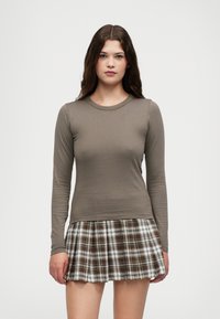 Brown long-sleeve top paired with a plaid skirt featuring white, brown, and black colors. Textured fabric with a fitted design and pleats.
