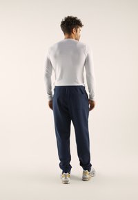 Valkoinen pitkähihainen paita yhdistettynä laivastonsinisiin joggereihin, joissa elastinen vyötärönauha ja takatasku, puettuna harmaiden ja keltaisten urheilukenkien kanssa.