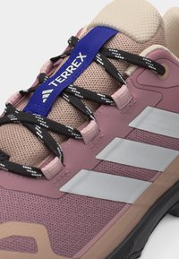 Ροζ και μπεζ παπούτσι Adidas Terrex με μαύρα και λευκά κορδόνια και λευκό λογότυπο με τρεις ρίγες στο πλάι.