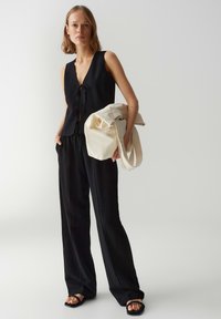 Zwart mouwloos topje met strikjes aan de voorkant, gecombineerd met losse zwarte broeken en een crèmekleurige tote bag. Glad materiaal met een minimalistisch ontwerp.