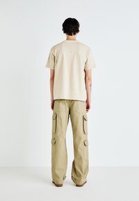 Beige Baumwoll-T-Shirt mit kurzen Ärmeln, kombiniert mit khakifarbenen Cargo-Hosen, die mehrere Taschen und eine lässige Passform bieten.
