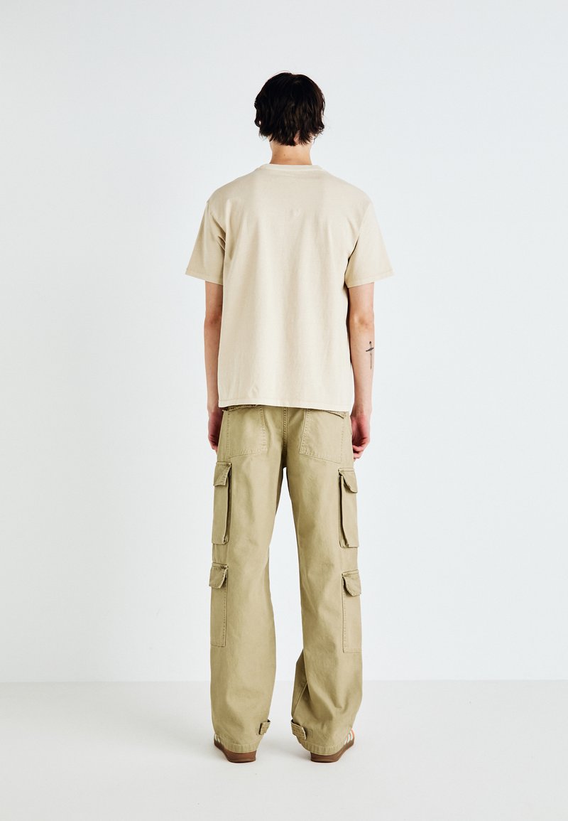 Camiseta de algodón beige de manga corta, combinada con pantalones cargo caqui que cuentan con múltiples bolsillos y un ajuste relajado.