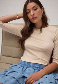 Beżowa prążkowana bluzka z długim rękawem w połączeniu z warstwową, jasnoniebieską spódnicą dżinsową. Strój posiada elastyczną talię i luźny krój. Złote akcenty bransoletki.