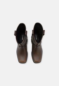 Bottines en cuir marron avec un bout carré, des sangles latérales et des détails de couture subtils. Fini lisse et semelle en caoutchouc pour plus de durabilité.