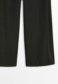 Donkergrijze pinstripe wijde broek, plat neergelegd, met de onderste helft van beide broekspijpen tegen een witte achtergrond.