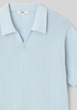 Polo en maille bleu clair à manches courtes avec col en V et col et poignets côtelés, étiquette de taille visible à l'intérieur du col.
